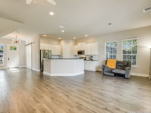 unfurnished living room featuring plenty of natural light, ceiling fan with notable chandelier, and light wood-type flooring