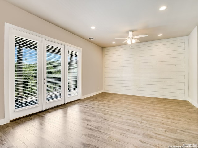 empty room with ceiling fan, wooden walls, and light hardwood / wood-style floors