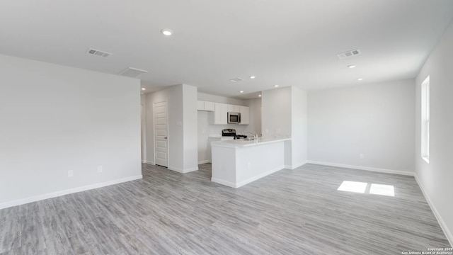 kitchen featuring stainless steel appliances, a wealth of natural light, light hardwood / wood-style floors, white cabinets, and kitchen peninsula