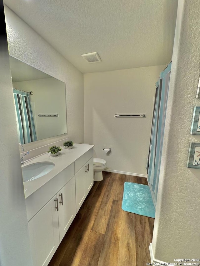 bathroom with hardwood / wood-style flooring, vanity, toilet, and a textured ceiling