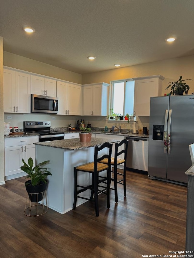 kitchen featuring a breakfast bar area, appliances with stainless steel finishes, white cabinetry, dark stone countertops, and a kitchen island