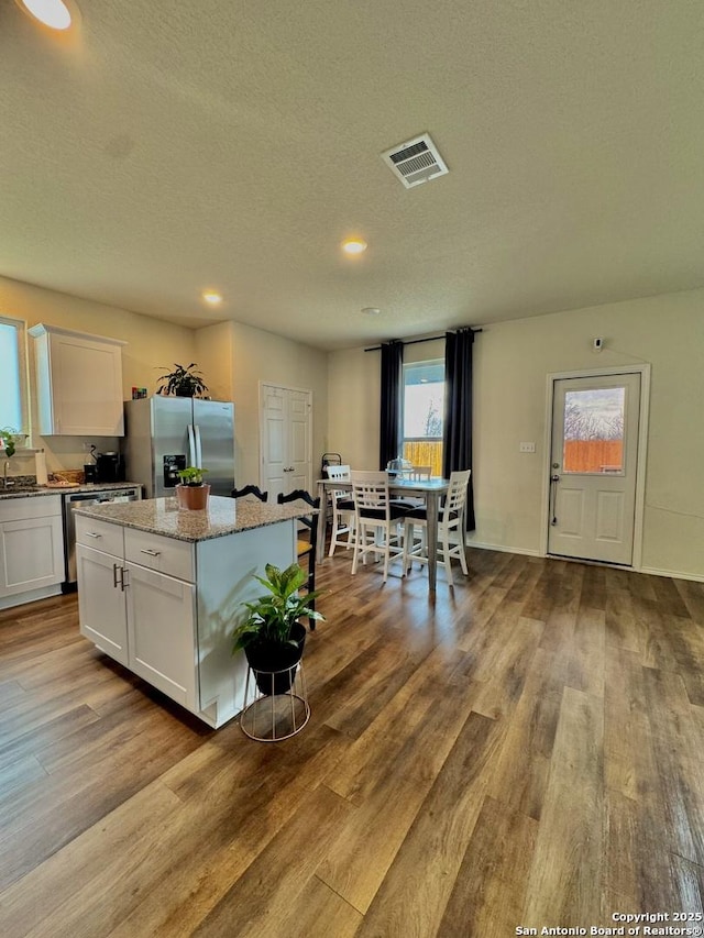 kitchen with appliances with stainless steel finishes, light stone countertops, a kitchen island, and white cabinets