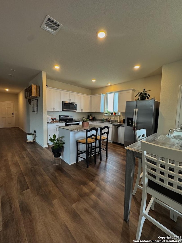 kitchen with dark wood-type flooring, a breakfast bar, appliances with stainless steel finishes, white cabinetry, and a kitchen island