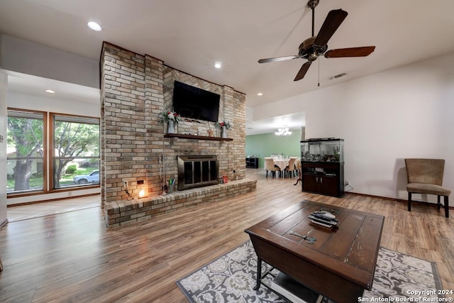 living room with ceiling fan with notable chandelier, a fireplace, and light hardwood / wood-style flooring