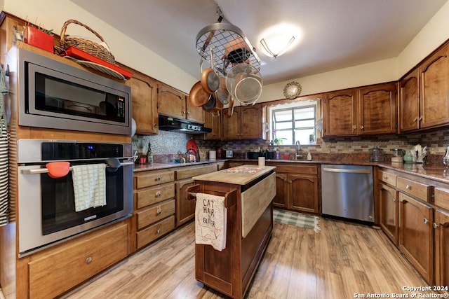 kitchen featuring appliances with stainless steel finishes, sink, light hardwood / wood-style flooring, and backsplash