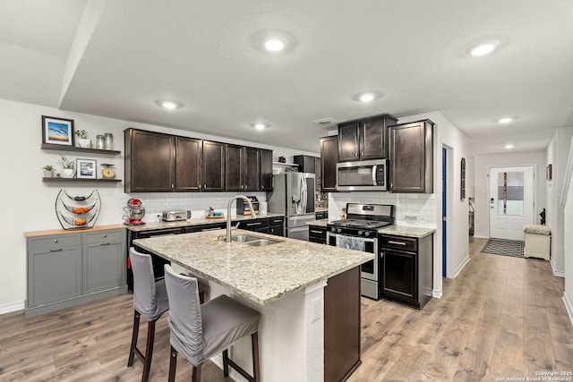 kitchen featuring appliances with stainless steel finishes, a breakfast bar, sink, a center island with sink, and light hardwood / wood-style flooring