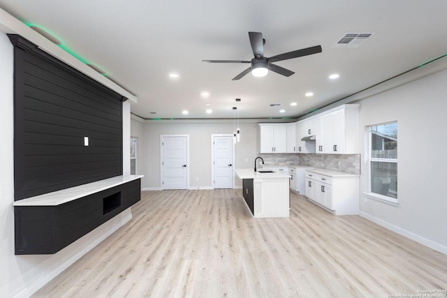 kitchen with white cabinetry, hanging light fixtures, tasteful backsplash, a center island with sink, and light wood-type flooring