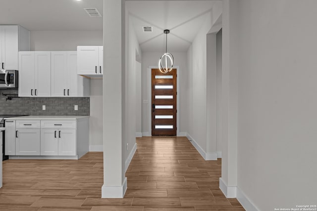 kitchen featuring white cabinetry, backsplash, pendant lighting, and light wood-type flooring