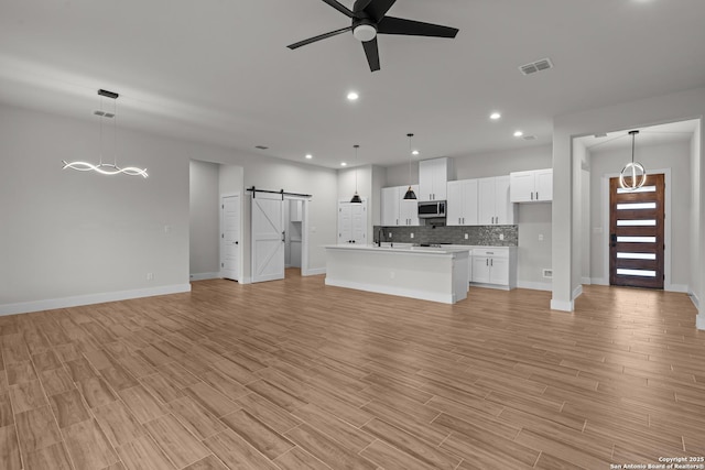 unfurnished living room with ceiling fan, a barn door, and light hardwood / wood-style floors