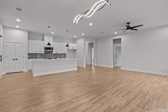 unfurnished living room with sink, light hardwood / wood-style flooring, and ceiling fan