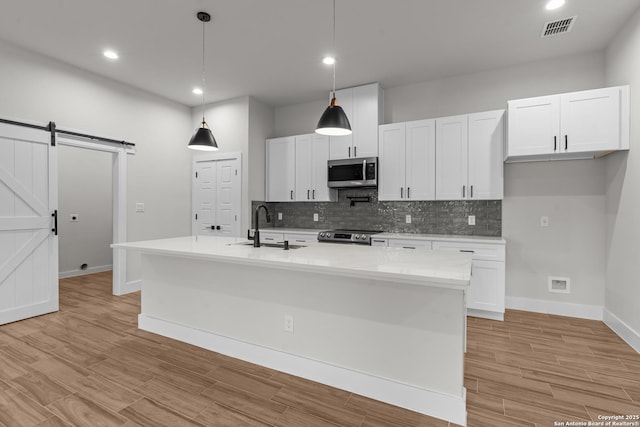 kitchen with a kitchen island with sink, a barn door, white cabinets, and appliances with stainless steel finishes