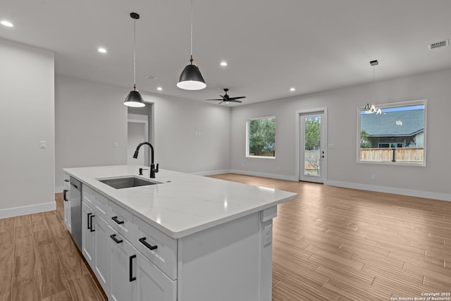 kitchen with sink, white cabinetry, a center island with sink, pendant lighting, and light stone countertops