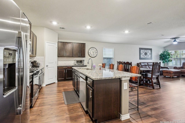 kitchen with dark hardwood / wood-style floors, tasteful backsplash, a kitchen breakfast bar, stainless steel appliances, and a center island with sink