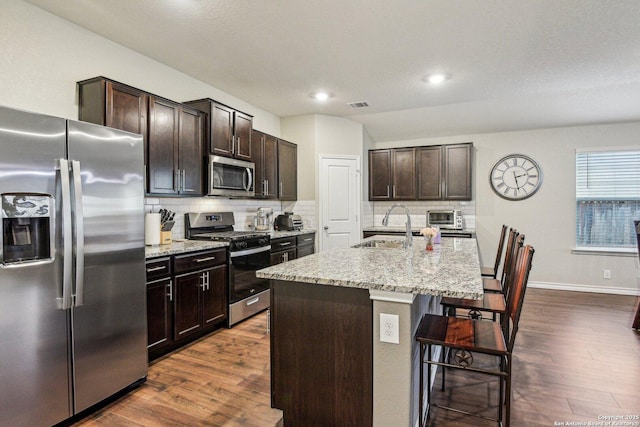 kitchen featuring a kitchen bar, sink, tasteful backsplash, appliances with stainless steel finishes, and an island with sink