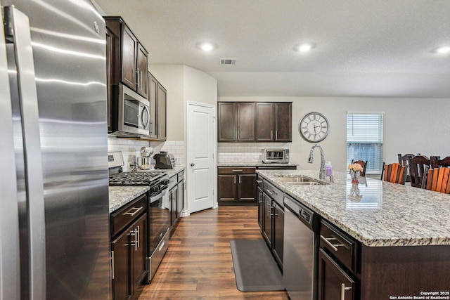 kitchen featuring dark hardwood / wood-style floors, sink, backsplash, stainless steel appliances, and a center island with sink