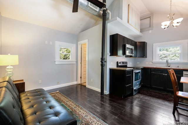 kitchen featuring dark wood-type flooring, high vaulted ceiling, hanging light fixtures, a notable chandelier, and stainless steel appliances