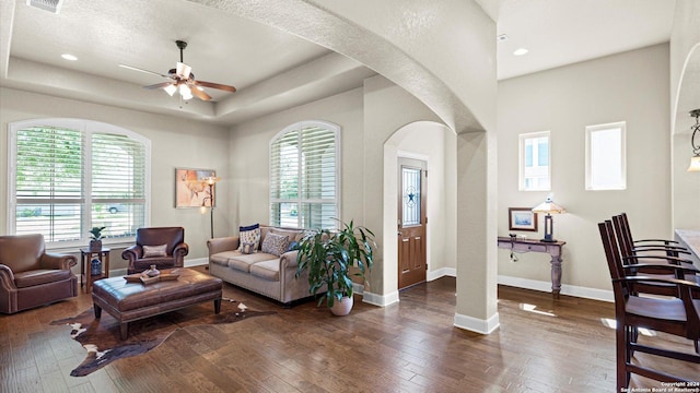 living room featuring ceiling fan, a tray ceiling, and dark hardwood / wood-style floors