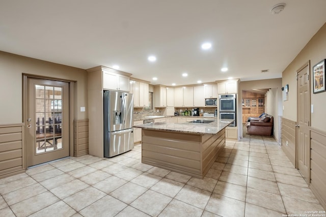 kitchen with light tile patterned floors, appliances with stainless steel finishes, a center island, light stone counters, and white cabinets