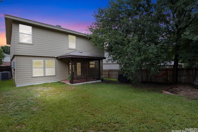 back house at dusk with central AC unit and a lawn