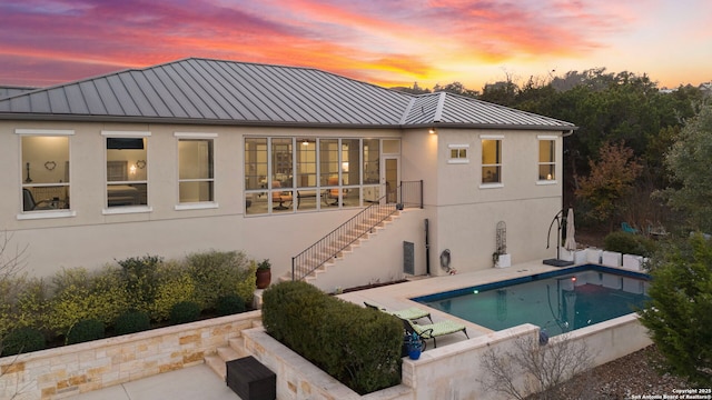 back of property at dusk featuring a standing seam roof, a patio area, metal roof, an outdoor pool, and stairs