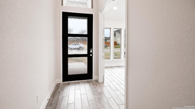 doorway to outside with a textured wall, baseboards, and wood finished floors