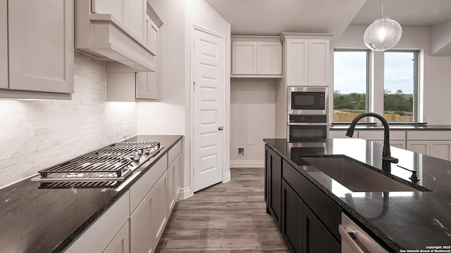 kitchen featuring dark stone counters, a sink, white cabinets, stainless steel appliances, and backsplash