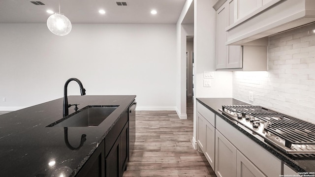 kitchen featuring dark stone countertops, wood finished floors, a sink, tasteful backsplash, and custom range hood