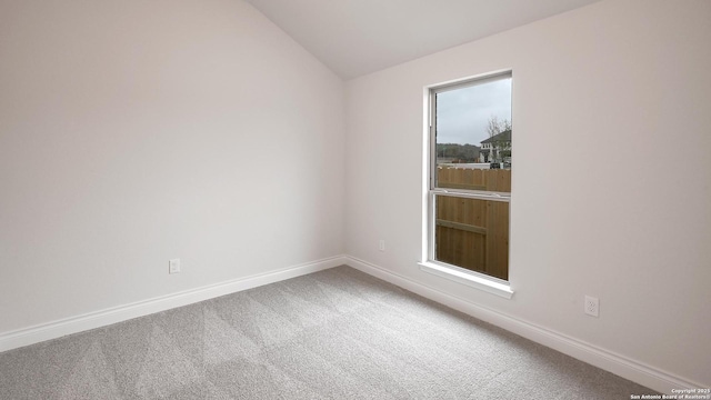 carpeted spare room with vaulted ceiling and baseboards