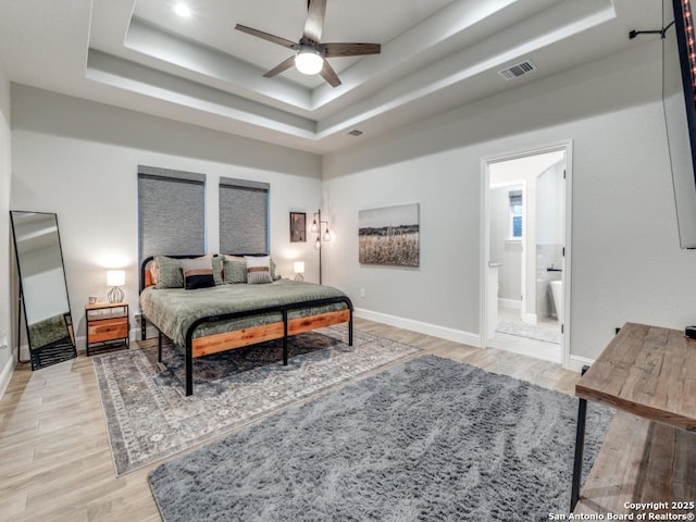 bedroom featuring a raised ceiling, ensuite bathroom, and light wood-type flooring