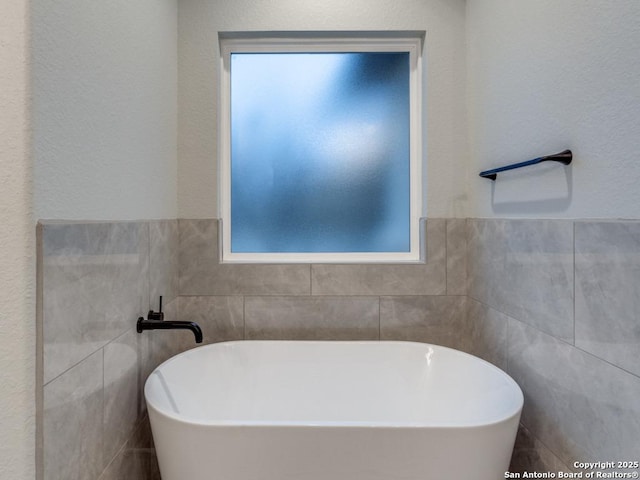 bathroom featuring tile walls, a bath, and plenty of natural light