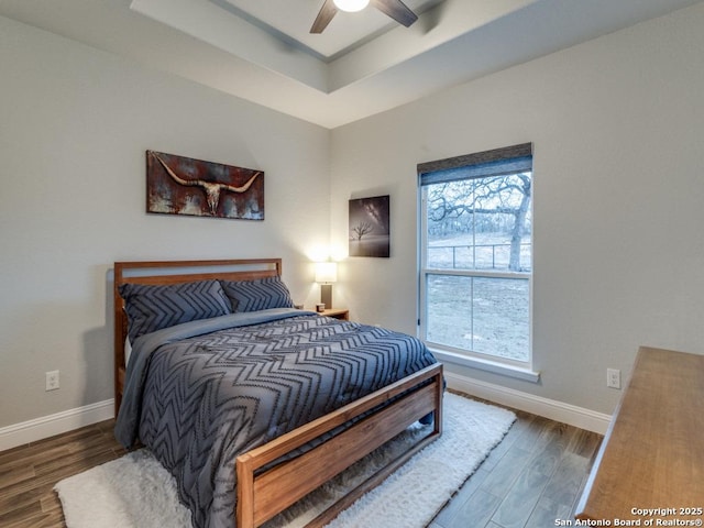 bedroom with a tray ceiling, dark hardwood / wood-style floors, and ceiling fan