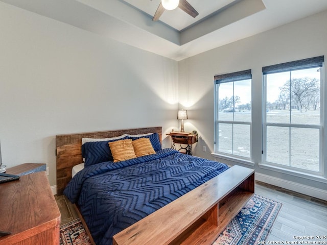 bedroom featuring multiple windows, hardwood / wood-style flooring, a raised ceiling, and ceiling fan