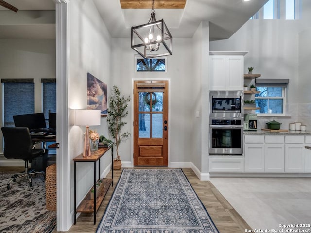 foyer entrance featuring a towering ceiling, a wealth of natural light, a notable chandelier, and light hardwood / wood-style flooring