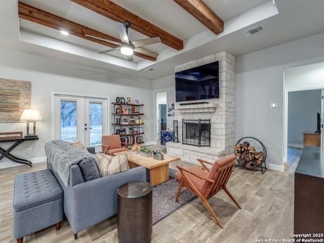 living room featuring french doors, a fireplace, light hardwood / wood-style flooring, and beamed ceiling