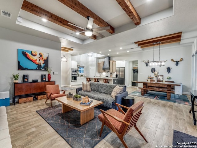 living room with ceiling fan, light hardwood / wood-style flooring, and beamed ceiling