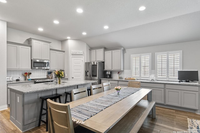 1905 High Bank, Seguin, TX 78155 - kitchen featuring stainless steel appliances, gray cabinets, decorative backsplash, vaulted ceiling, and a kitchen island with sink