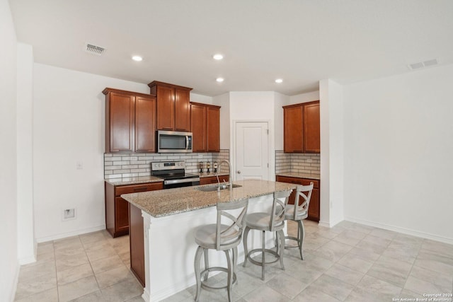 kitchen with sink, stainless steel appliances, a kitchen breakfast bar, light stone counters, and a center island with sink