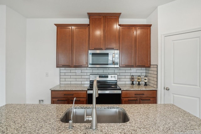 kitchen with stainless steel appliances, tasteful backsplash, sink, and light stone counters