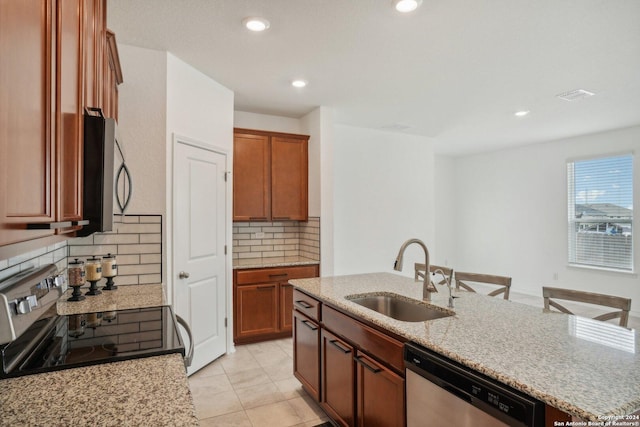 kitchen featuring appliances with stainless steel finishes, sink, decorative backsplash, a kitchen island with sink, and light stone counters