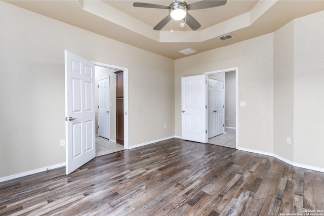 unfurnished bedroom with ceiling fan, wood-type flooring, and a tray ceiling