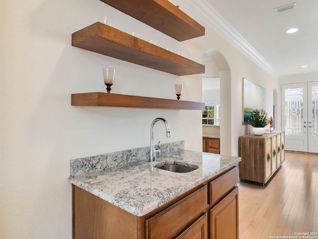 kitchen with french doors, sink, light stone counters, crown molding, and light hardwood / wood-style floors