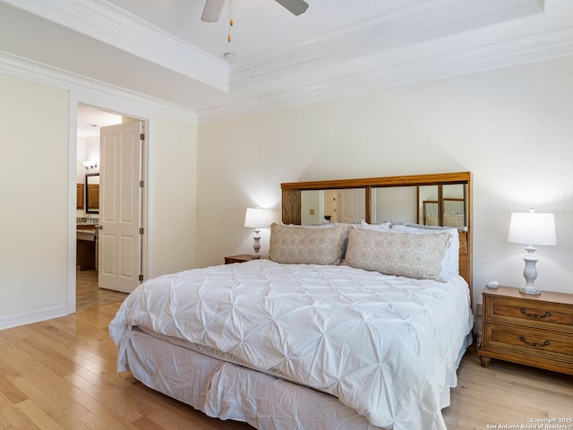 bedroom with ceiling fan, a tray ceiling, crown molding, ensuite bath, and light hardwood / wood-style flooring