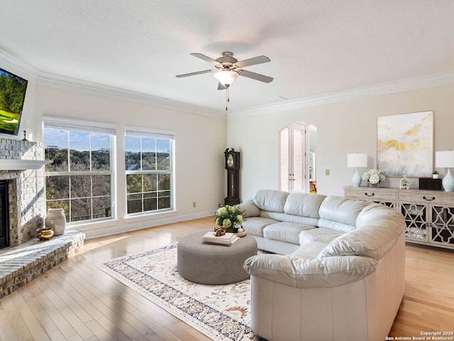 living room featuring a brick fireplace, a textured ceiling, ornamental molding, ceiling fan, and light hardwood / wood-style floors