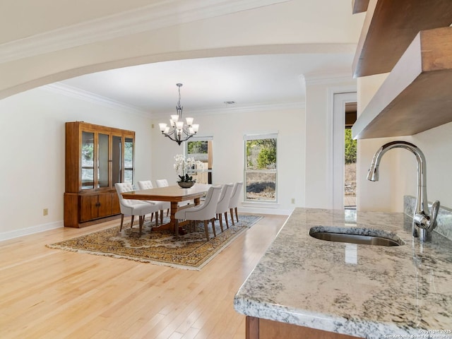 dining area with sink, a notable chandelier, ornamental molding, and light hardwood / wood-style floors