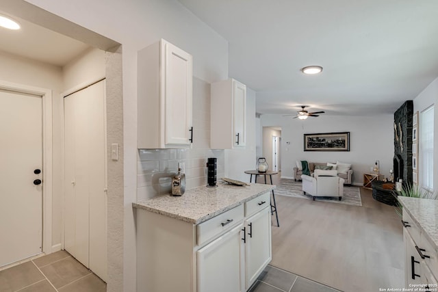 kitchen featuring ceiling fan, white cabinetry, backsplash, light stone counters, and light wood-type flooring