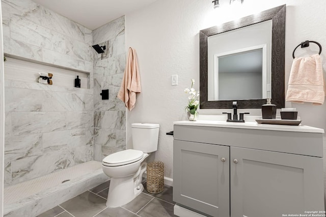 bathroom with tiled shower, vanity, toilet, and tile patterned flooring