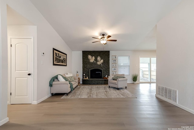 living room featuring ceiling fan, lofted ceiling, a fireplace, and light wood-type flooring