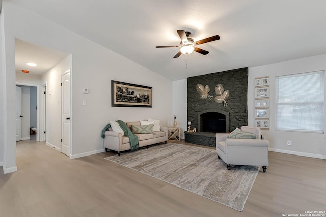 living room featuring lofted ceiling, a fireplace, ceiling fan, and light wood-type flooring