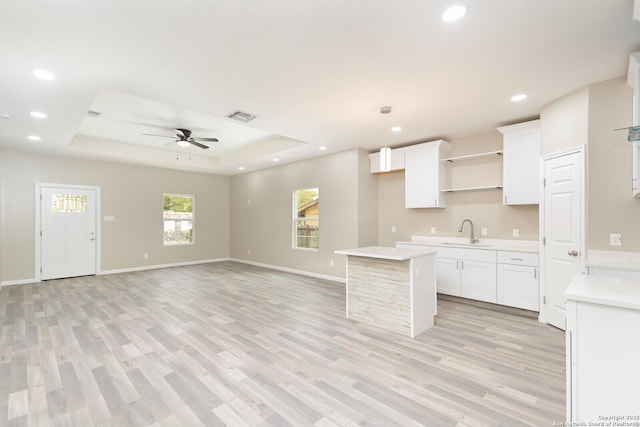 kitchen featuring sink, a raised ceiling, pendant lighting, light hardwood / wood-style floors, and white cabinets