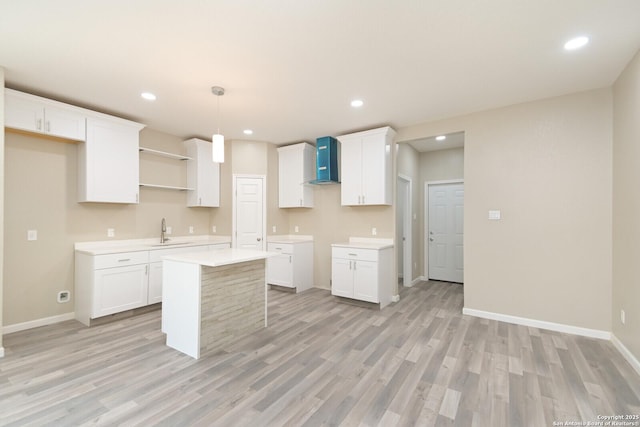 kitchen featuring wall chimney range hood, white cabinetry, hanging light fixtures, a center island, and light hardwood / wood-style floors